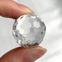 Hand holding a pure 23mm faceted crystal sphere to show its scale and perfect clarity.