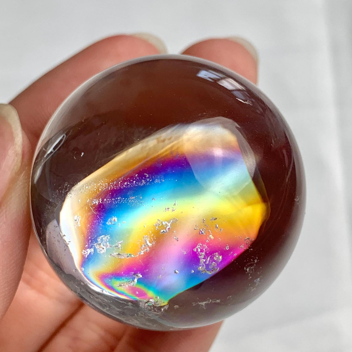 Small high clarity rainbow quartz sphere with polished reflective surface and natural inclusions
