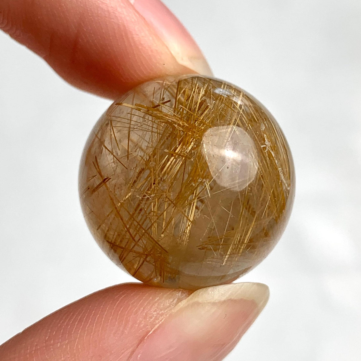 Small rutilated quartz sphere with glowing golden rutile threads inside