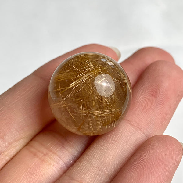 Clear quartz sphere showing soft golden rutile light reflections
