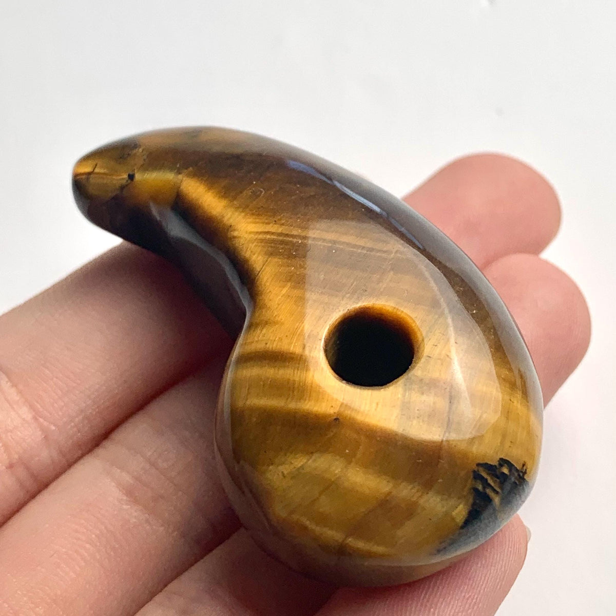Handheld photo displaying the size and rich luster of the carved Tiger Eye magatama stone.