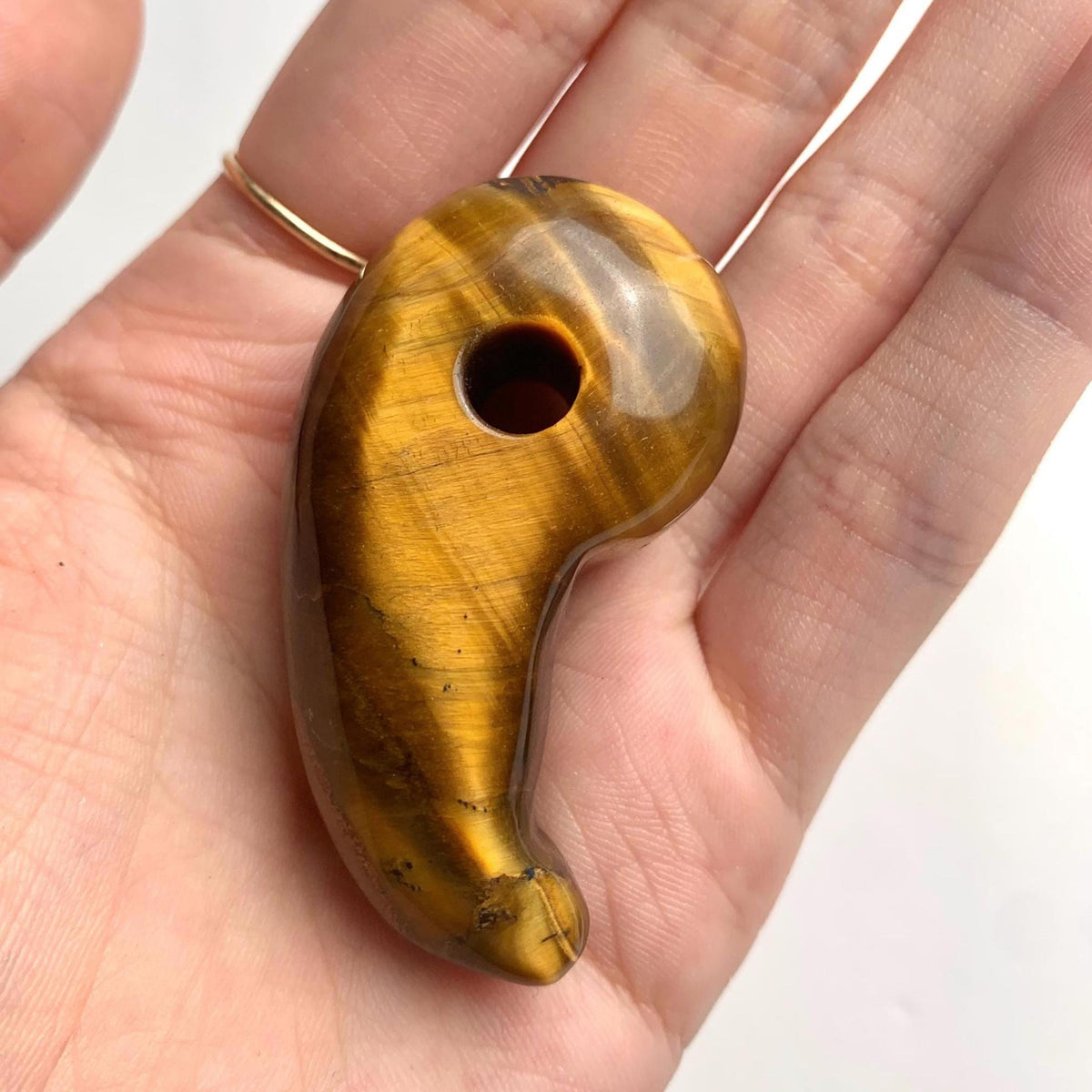 Handheld photo displaying the size and rich luster of the carved Tiger Eye magatama stone.