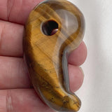 Handheld photo displaying the size and rich luster of the carved Tiger Eye magatama stone.
