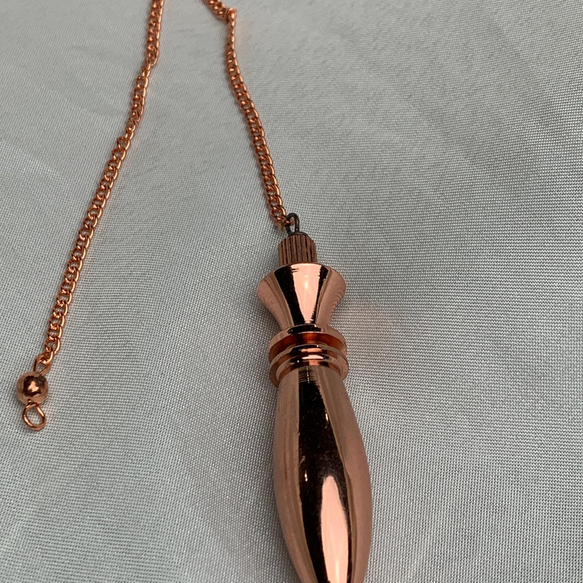 Copper pendulum with chain shown full length, chain draped, reflective reddish-brown pure copper dowsing pendulum