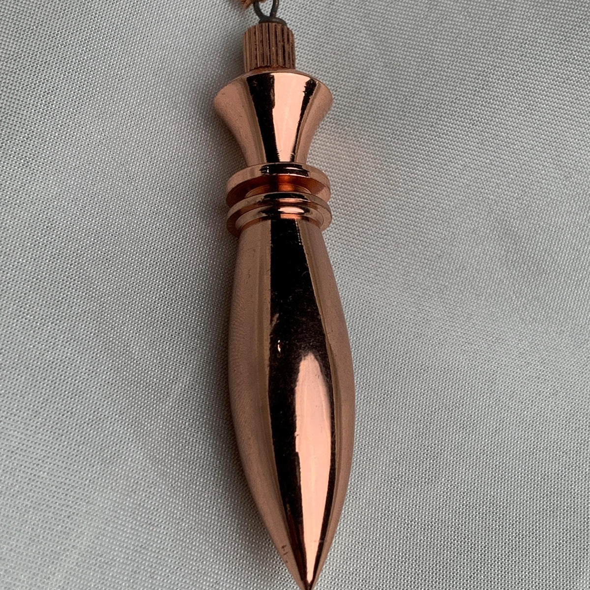 Close side detail of the cap and ring on a pure copper pendulum, sleek spindle profile for scrying and divination