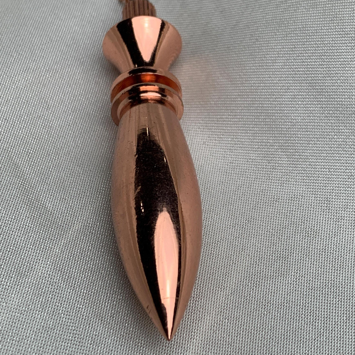 Vertical angled shot of the pointed tip and mirror-like surface, classic witchcraft pendulum look in warm copper