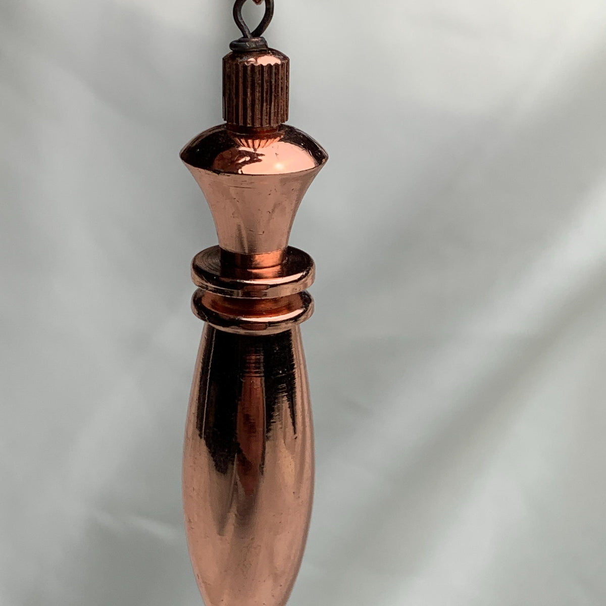 Tight frontal view highlighting faceted top and tapered point of a pure copper pendulum, ideal as a dowsing tool