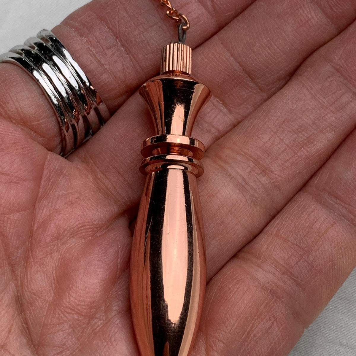 Handheld scale view, pure copper pendulum resting in palm, shows size, shine, and copper pendulum with chain detail
