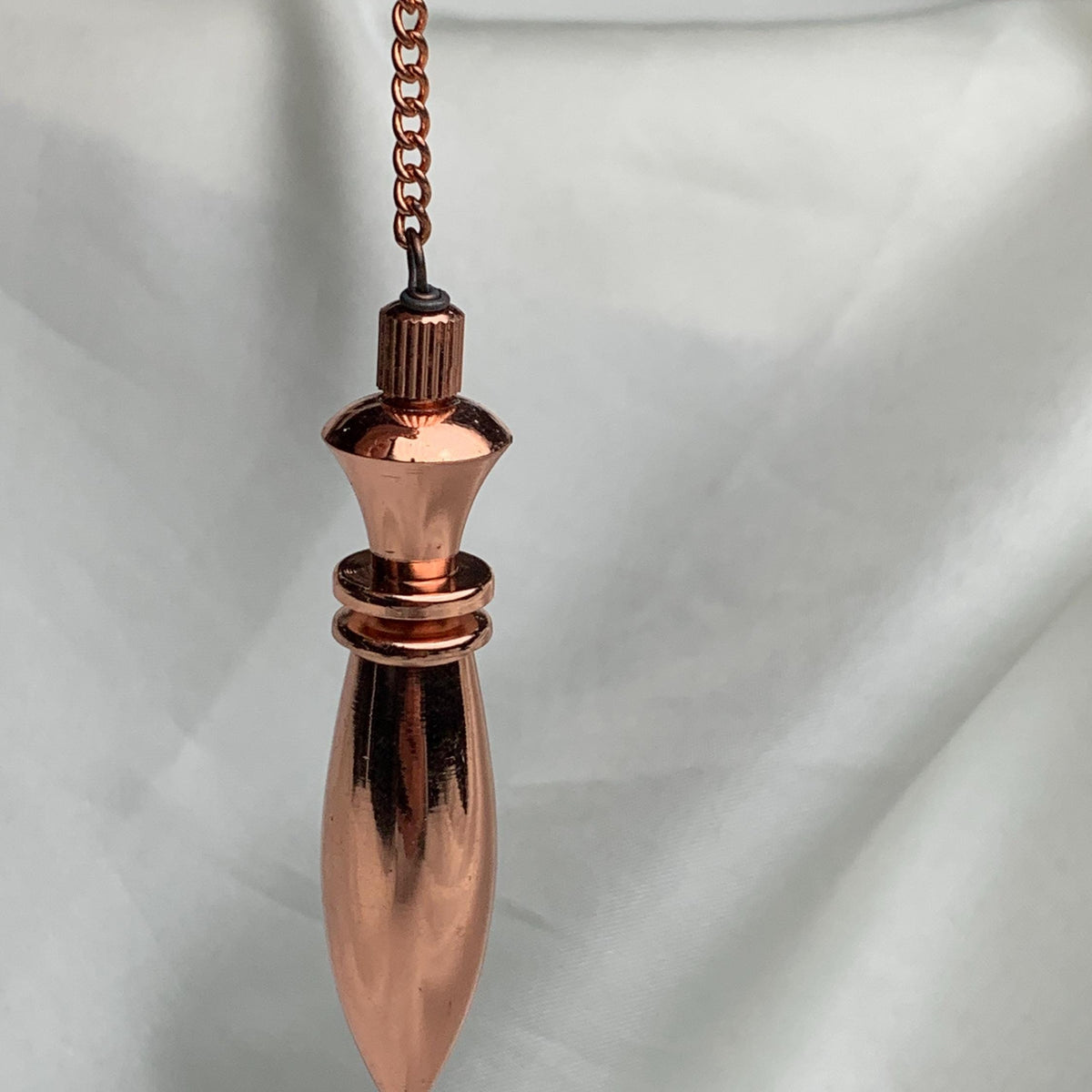 Hanging view with chain extending upward, traditional divination pendulum in polished copper, thoughtful 7th anniversary gift idea