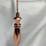 Hanging view with chain extending upward, traditional divination pendulum in polished copper, thoughtful 7th anniversary gift idea