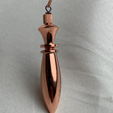 Isolated on smooth fabric, long pointed pure copper pendulum paired with matching chain, simple traditional divination tool
